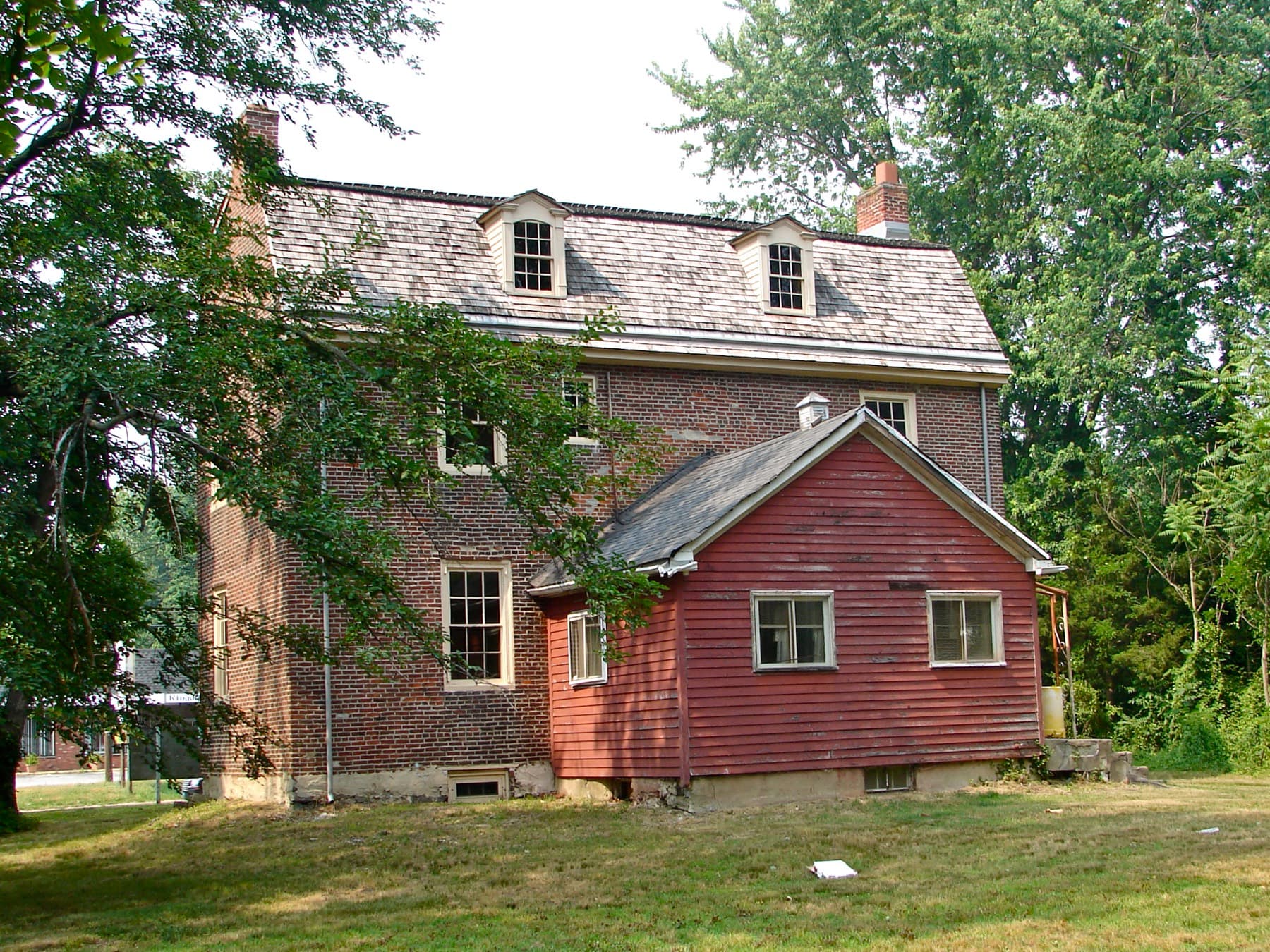 A brick colonial farmhouse with a red clapboard addition, surrounded by trees